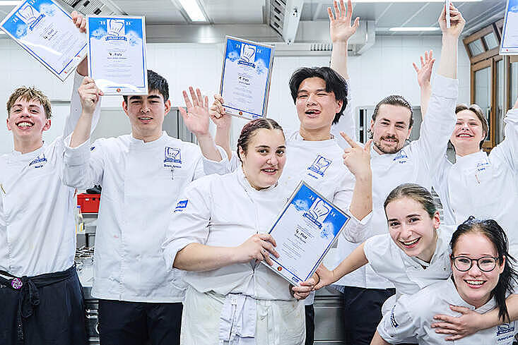 Die Finalisten des MILRAM Cup 2026 stehen gemeinsam mit Jury und Organisatoren nach der Siegerehrung auf der Bühne. Der Nachwuchs-Kochwettbewerb fand in Bremen statt.