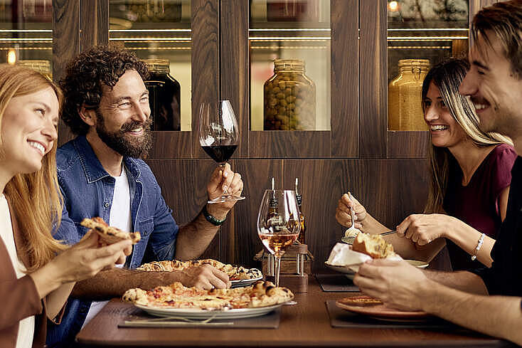 Gruppe von Restaurantgästen sitzt gemeinsam am Tisch und unterhält sich beim Essen in einem Innenraum.