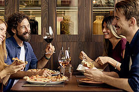 Gruppe von Restaurantgästen sitzt gemeinsam am Tisch und unterhält sich beim Essen in einem Innenraum.