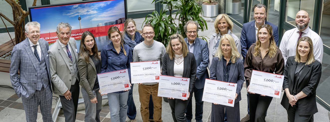 Gruppe von Vertreterinnen und Vertretern der Klüh-Unternehmensgruppe sowie sozialer Initiativen bei einer Scheckübergabe in Düsseldorf, mehrere Personen halten Spendenschecks über jeweils 5.000 Euro.